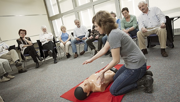 Female giving demonstration on how to give CPR in front of middle aged crowd