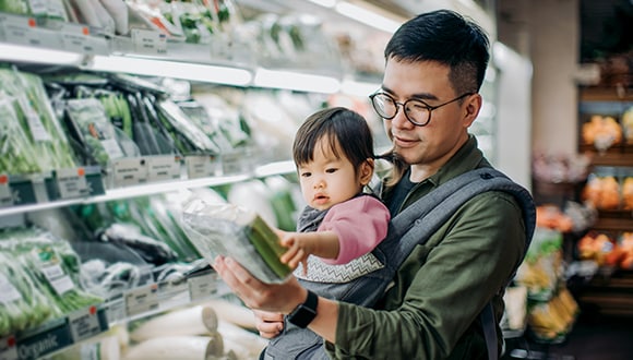 A father with a young baby reads the food labelling at the grocery store