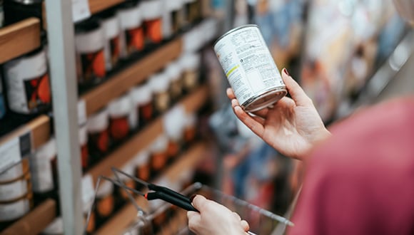 A person in a supermarket reading the food labelling on canned goods