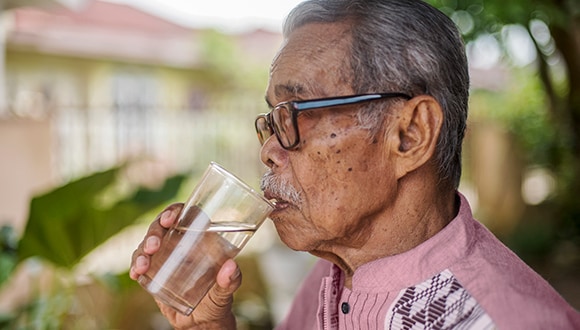 A man drinking a glass of water, excessive water consumption being a diabetes symptom
