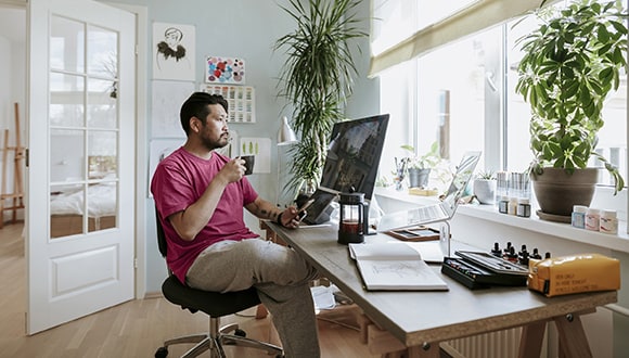 Man sitting at a desk in an office with a coffee looking at a computer
