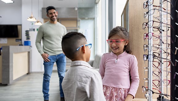 father watches as two children try on glasses