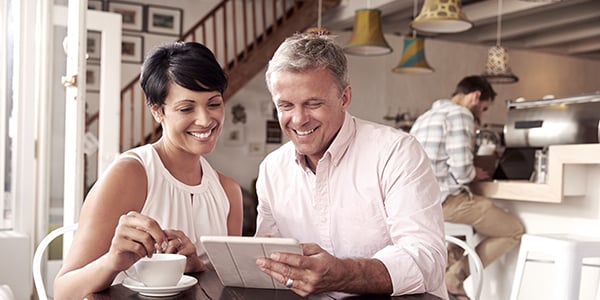 Two people sitting at a table looking at a tablet screen and smiling