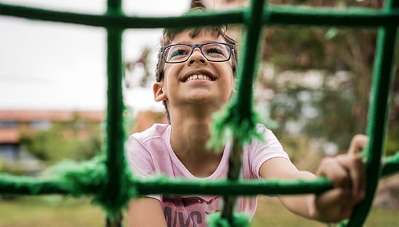 Building confidence in children: Happy young boy climbing playground netting.