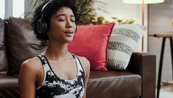 Breathing exercises can help reduce anxiety: Woman with headphones on in living room doing breathing exercises