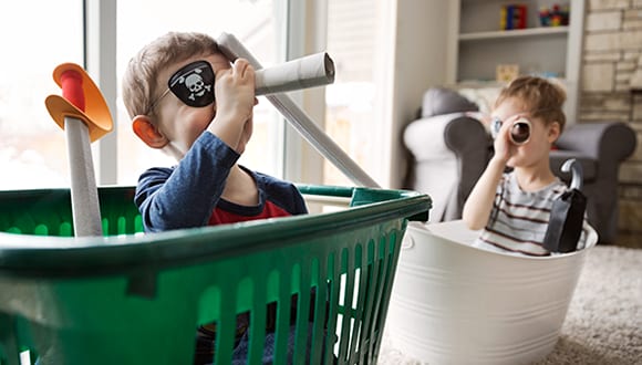 Two children sitting in laundry baskets pretending to be pirates and looking through telescopes