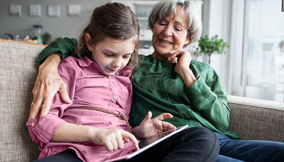 Common symptoms of depression: grandmother with her arms around granddaughter looking at a book on sofa.