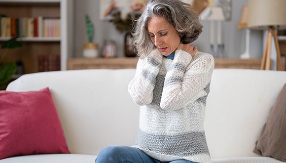 Woman holding her neck, sitting on the couch in pain showing signs of heart attack