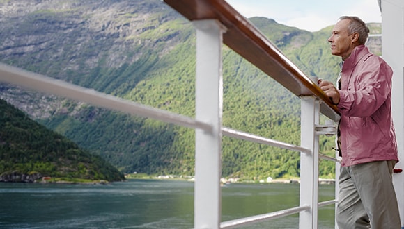 Man travelling, standing at a railing looking at water and moutains