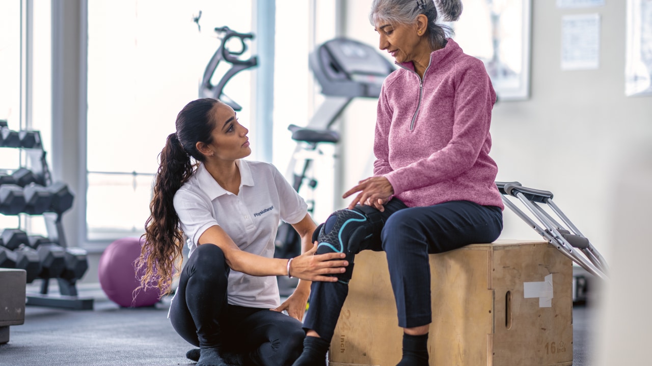 A woman in a gym getting her joint pain assessed by a physio.
