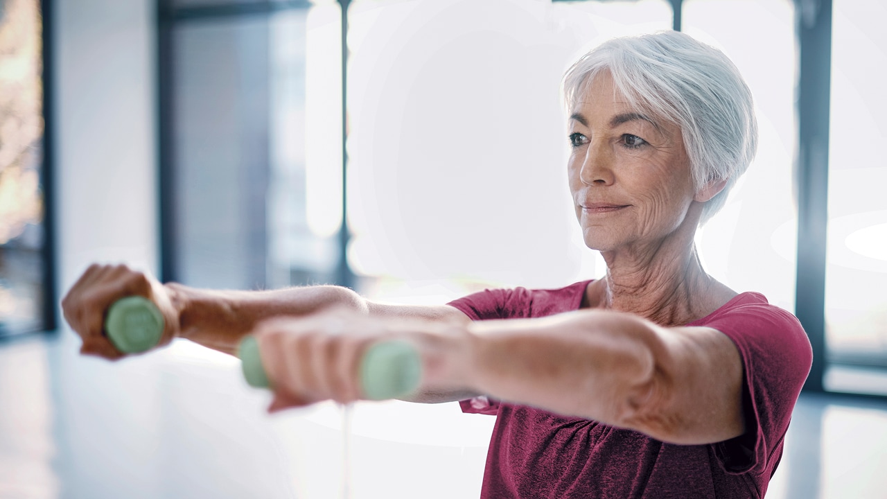 An elderly woman exercising with weights held out in front of her.