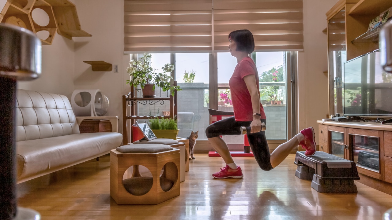 A woman exercising in the living room of her home with weights and lunges.