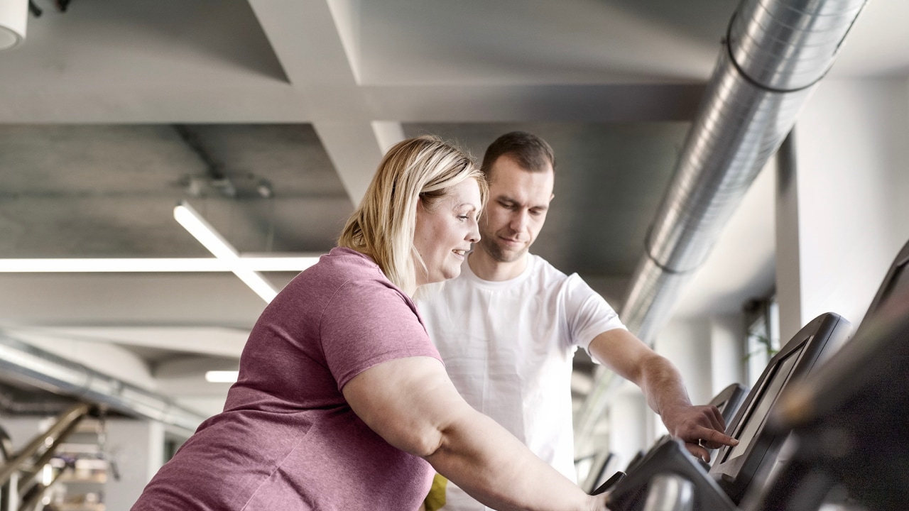 A woman exercising on a treadmill with a personal trainer beside her.