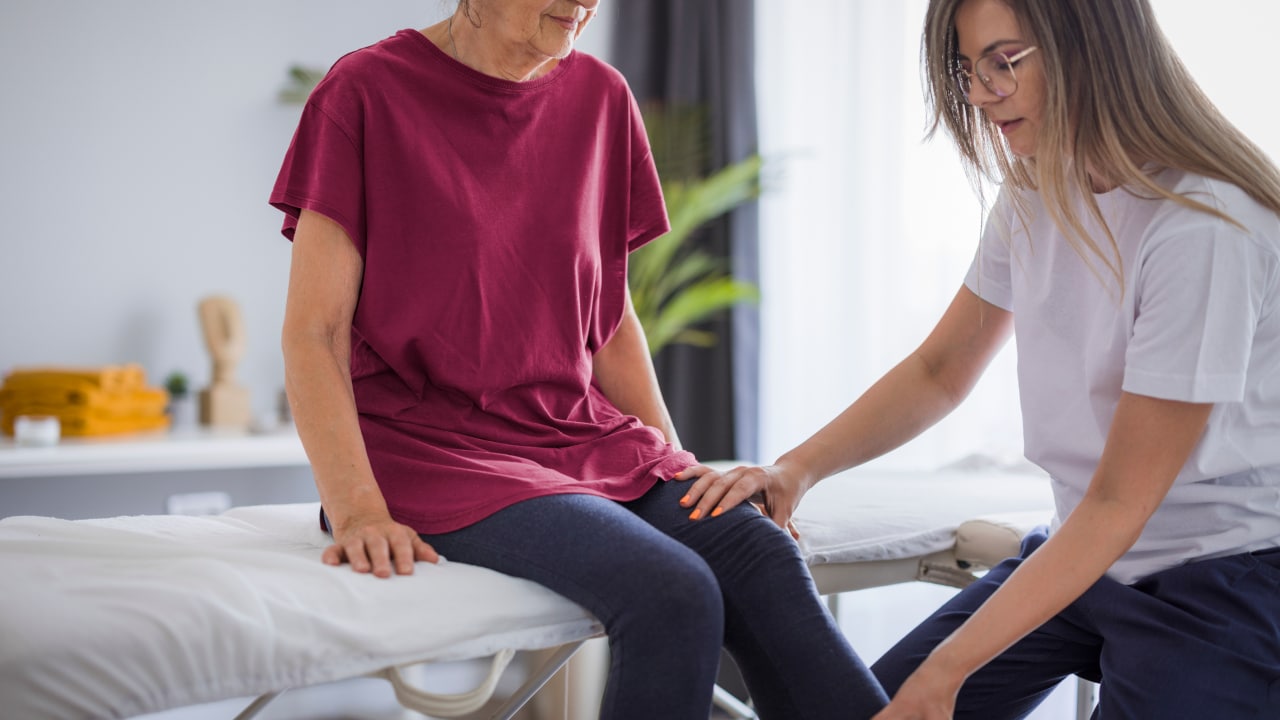 Woman sitting on therapy table getting treatment for her knee joint pain.