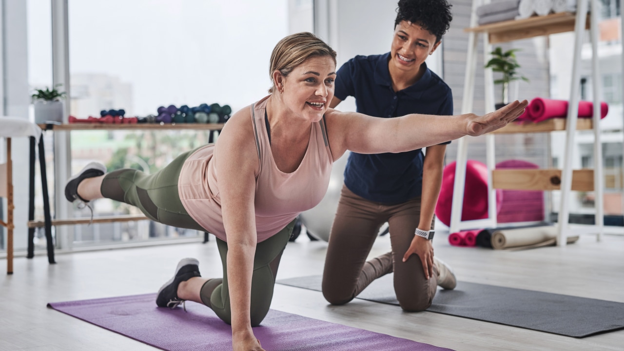 A woman exercising on a gym mat with a personal trainer next to them.