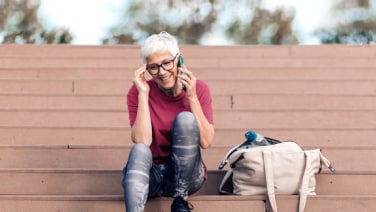 A middle aged woman with short hair sits on steps, talking on her phone and smiling.