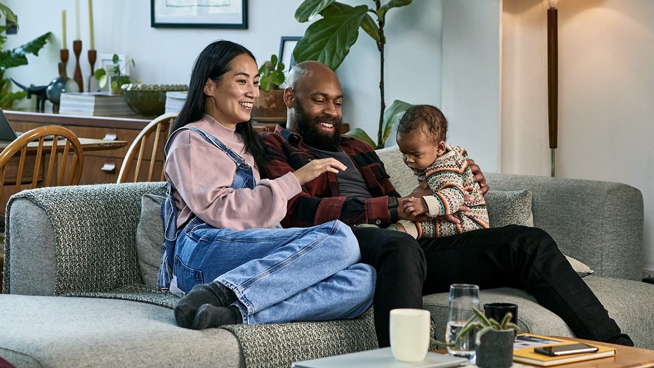 A couple sitting on the lounge smiling with their young child.