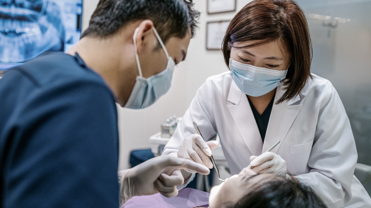 A female dentist and male dental assistant conduct a dental check-up on a patient.