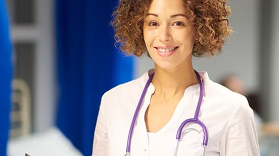 A female doctor smiling wearing a stethoscope in a hospital.
