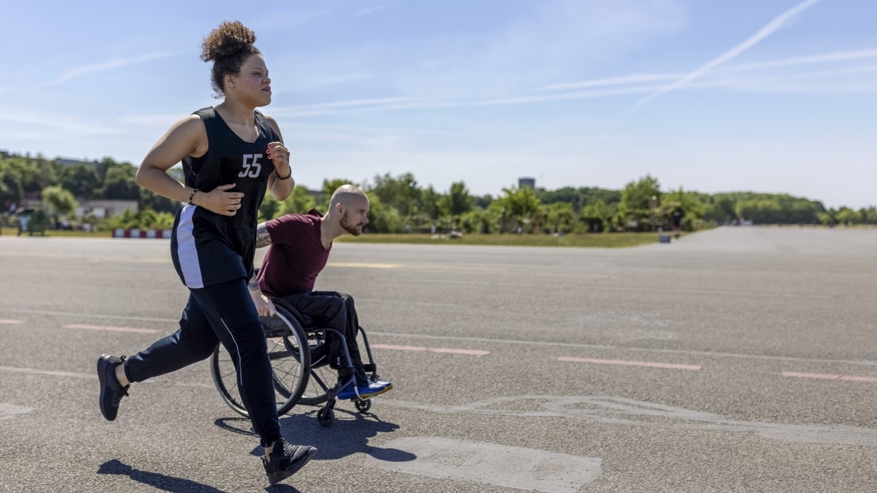 Friend running beside man in wheelchair.