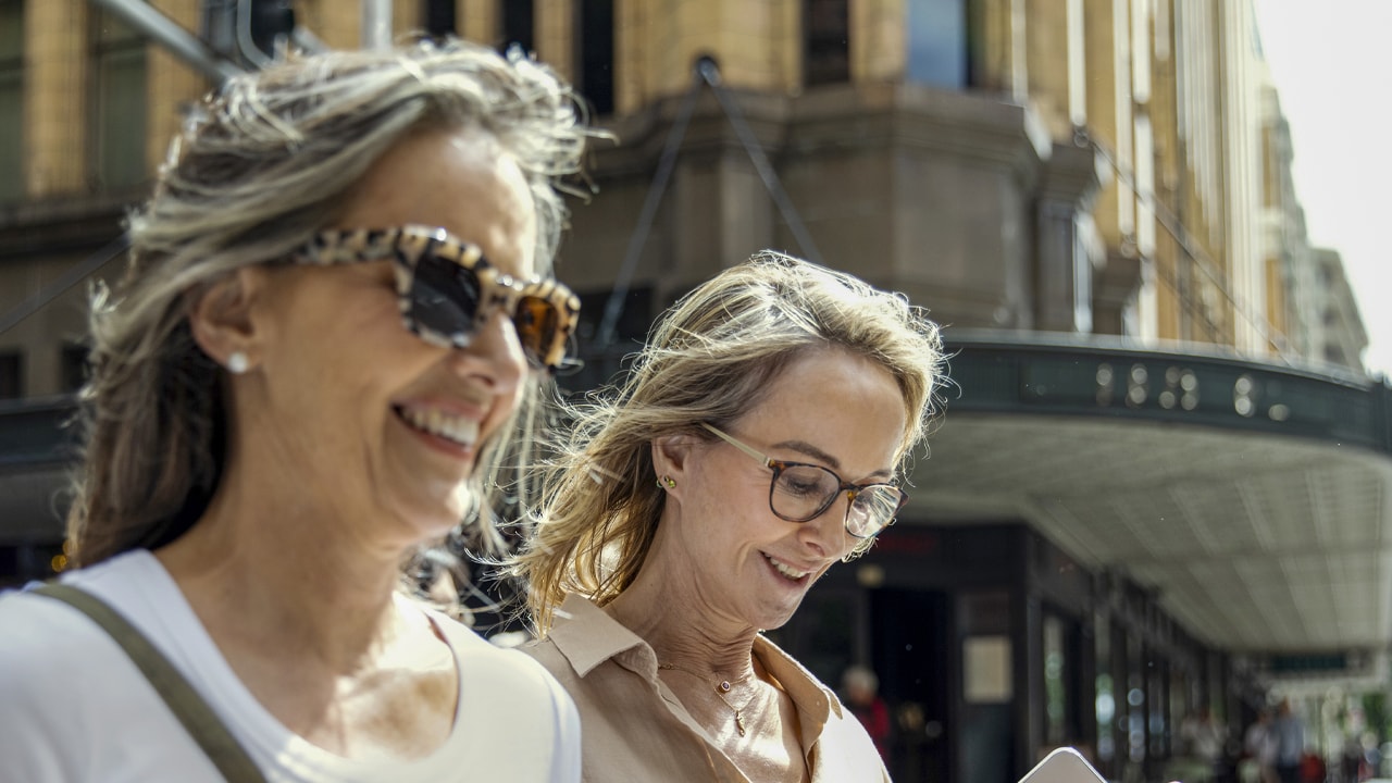 Two female friends wearing glasses walking along some streets in the inner city.