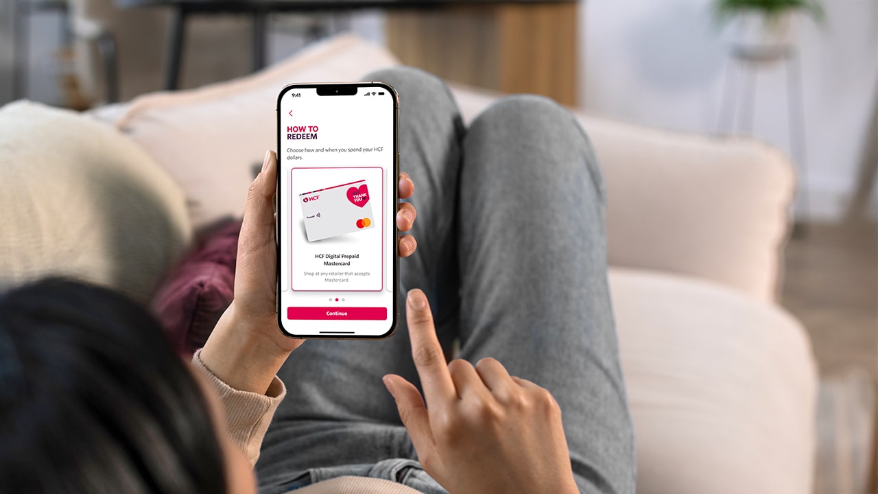 Woman sitting on the lounge looking at the HCF Thank You app on her mobile.