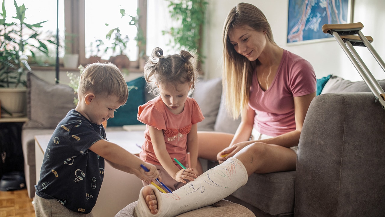 A lady with a broken leg sitting on the lounge with her kids.