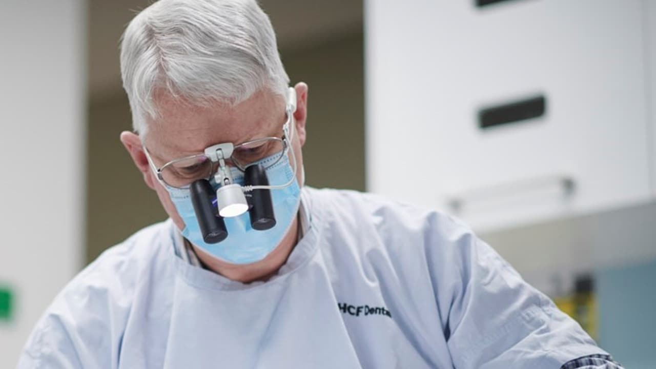 A male dentist wearing dental loupes conducting a dental check-up on a patient.