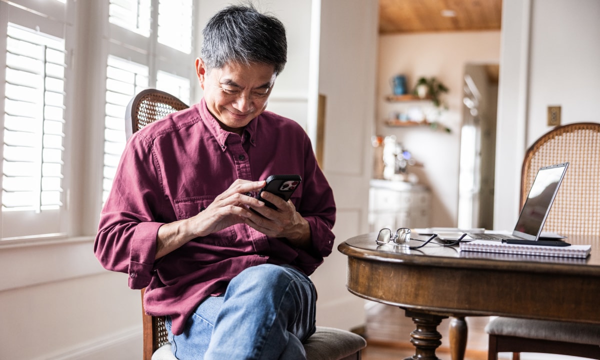 Man browsing his smartphone while sitting in the dining room.