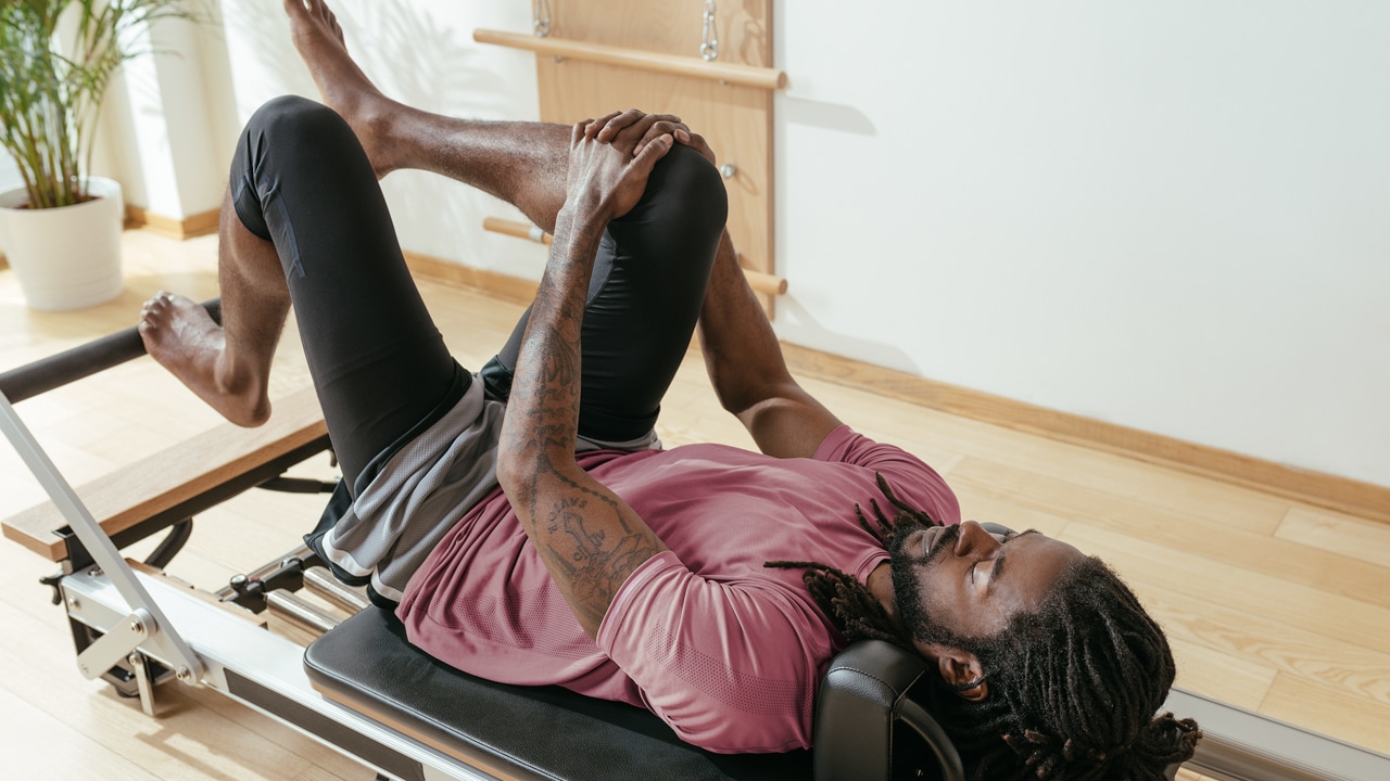 A man stretching his legs while lying on a Pilates reformer.