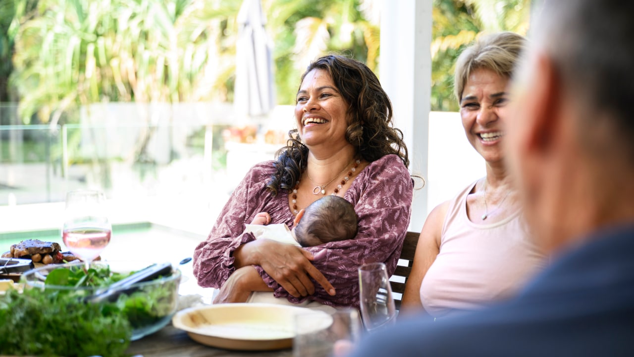 A mother sitting with friends nursing a baby.