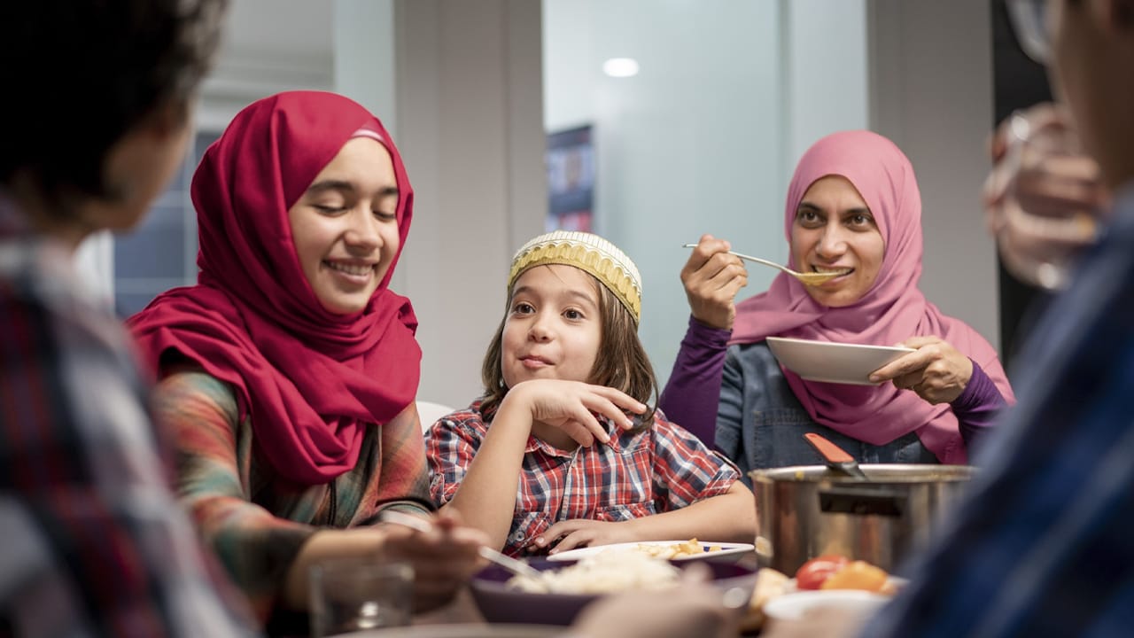 A multicultural family has dinner together while sitting at the dining table.