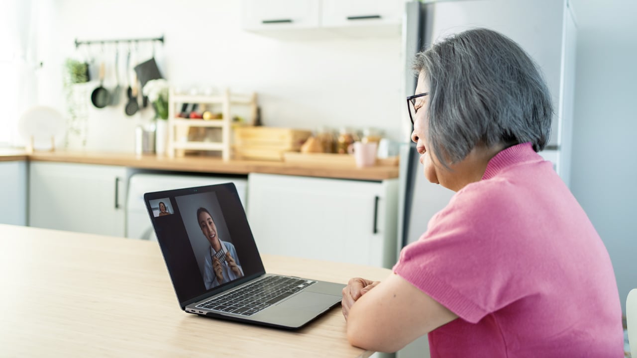 An older woman using a laptop while speaking to a medical professional through a video call.