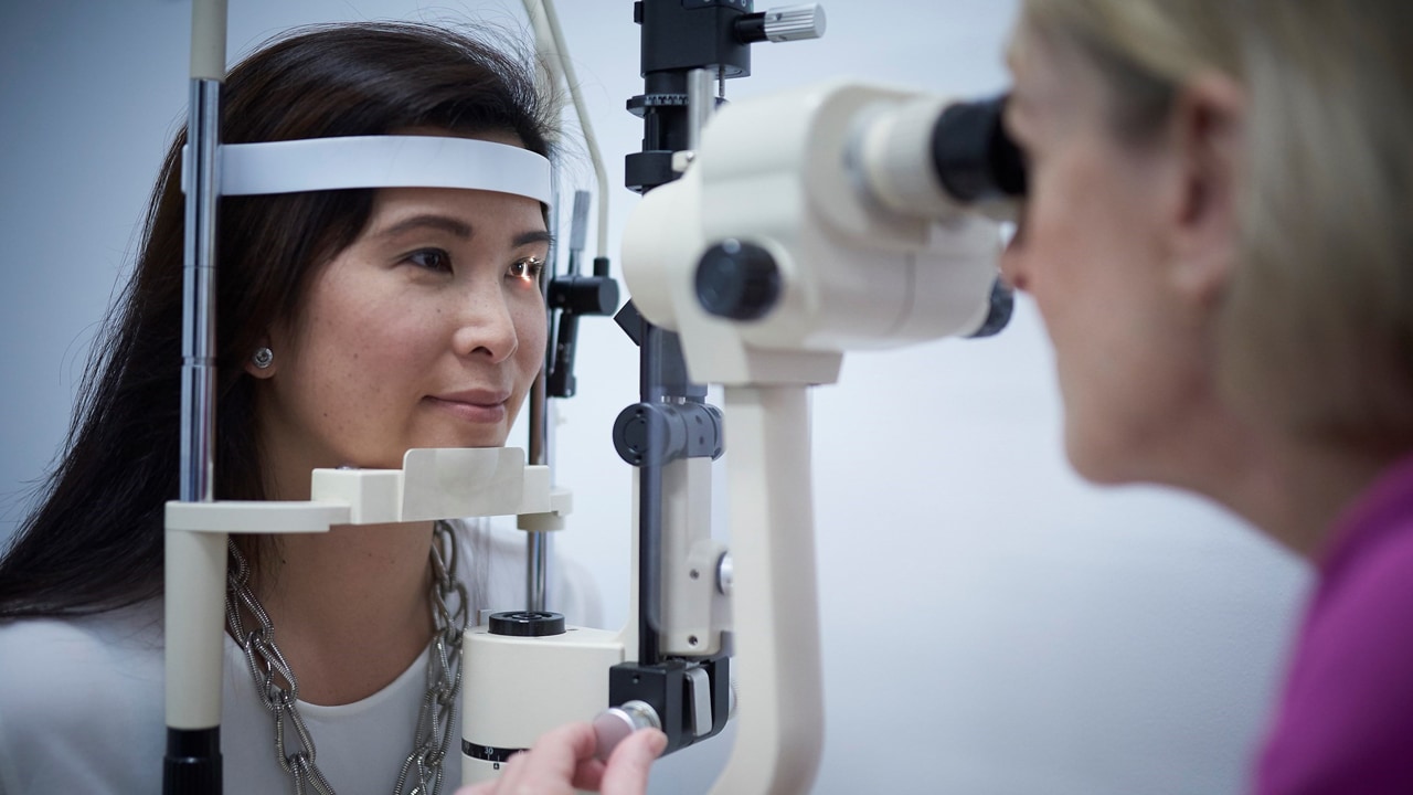 An optometrist conducts an eye exam on a female patient using a Frey slit lamp.