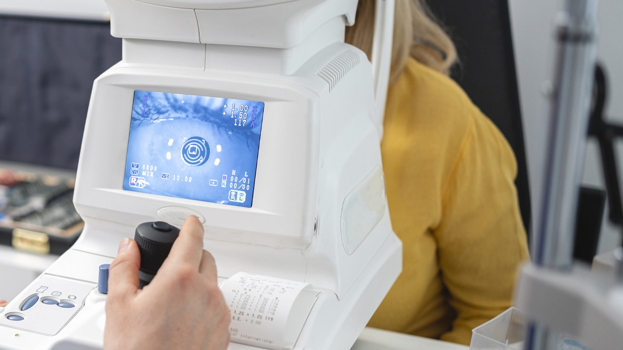 A male optometrist scans a patient's eyes for myopia using an optical biometer.