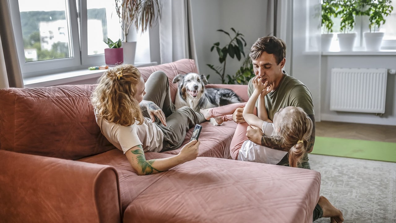 Parents playing in the lounge room with their child and pet dog.