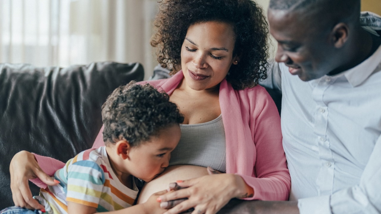 Pregnant woman sitting on lounge with partner and son.