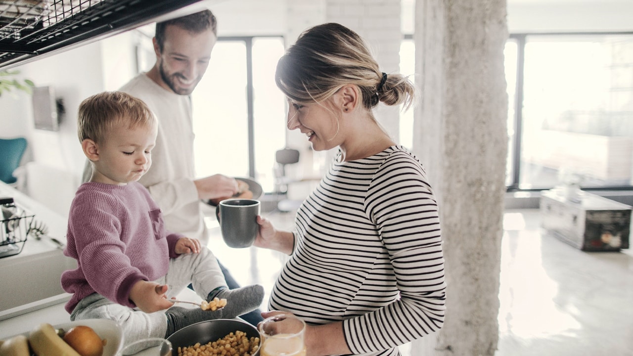 pregnant woman cooking breakfast with husband and toddler.