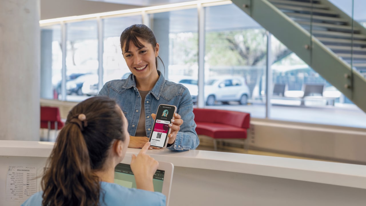 A woman showing her smartphone and QR code to a receptionist.