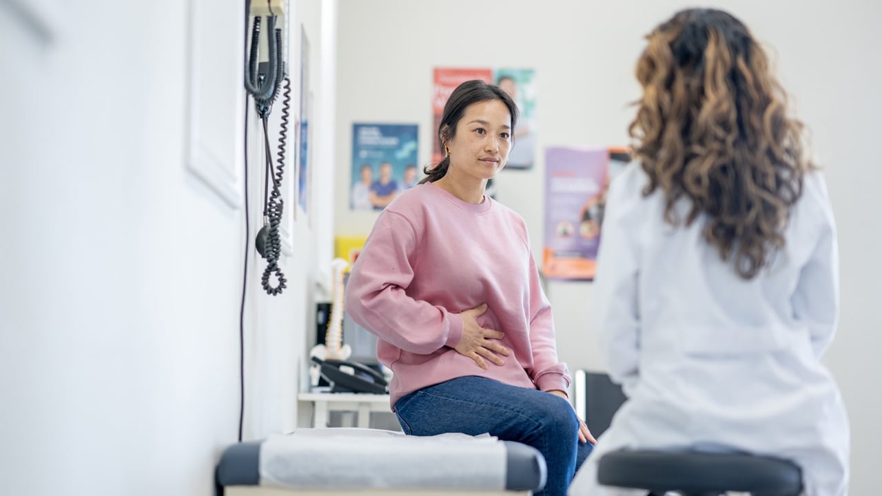 An Asian woman sitting on an examanation bed talking to a doctor.