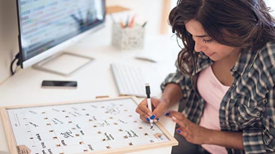 A woman sitting at a desk ticking and crossing a calendar.