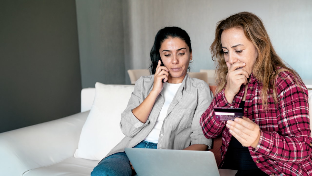 A photo of two women checking their phones for possible digital fraud activity.