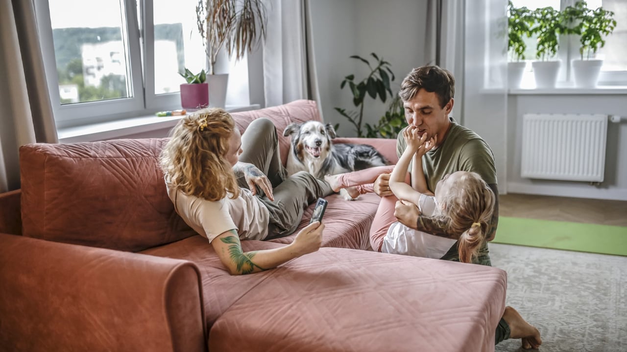 A photo of a young family playing on the couch at home with their dog.