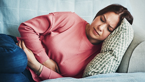 Woman with PCOS symptoms lying on couch holding stomach in pain