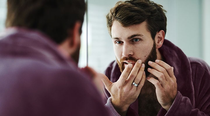 Man checking his skin in the mirror: Adult acne is often caused by hormones