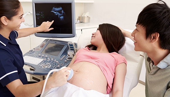  Woman getting an ultrasound, which is one of the many tests during pregnancy, with her partner beside her. 