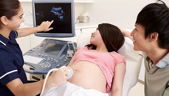 Woman getting an ultrasound, which is one of the many tests during pregnancy, with her partner beside her.