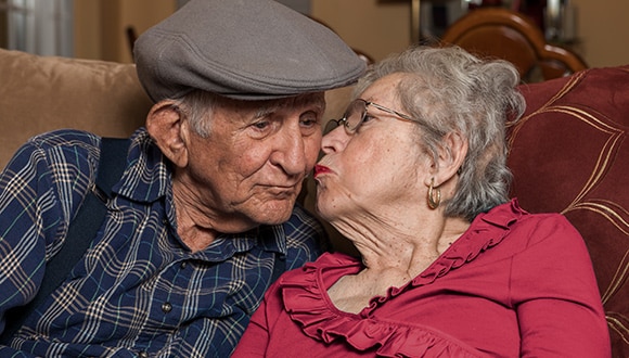 Elderly man and woman kissing on the couch