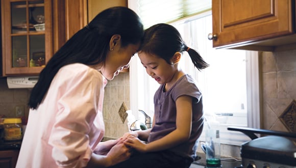 mother talking to young child sitting on kitchen bench