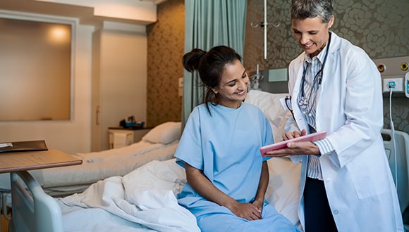 Woman sitting in hospital bed talking to a doctor about gap charges